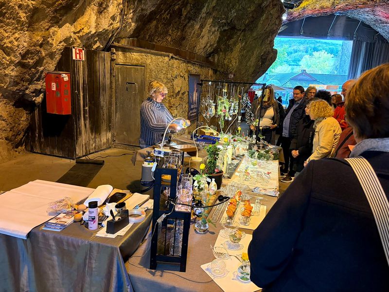 Glasbläserin an ihrem Stand, im Hintergrund der Blick aus der Höhle ins Grüne