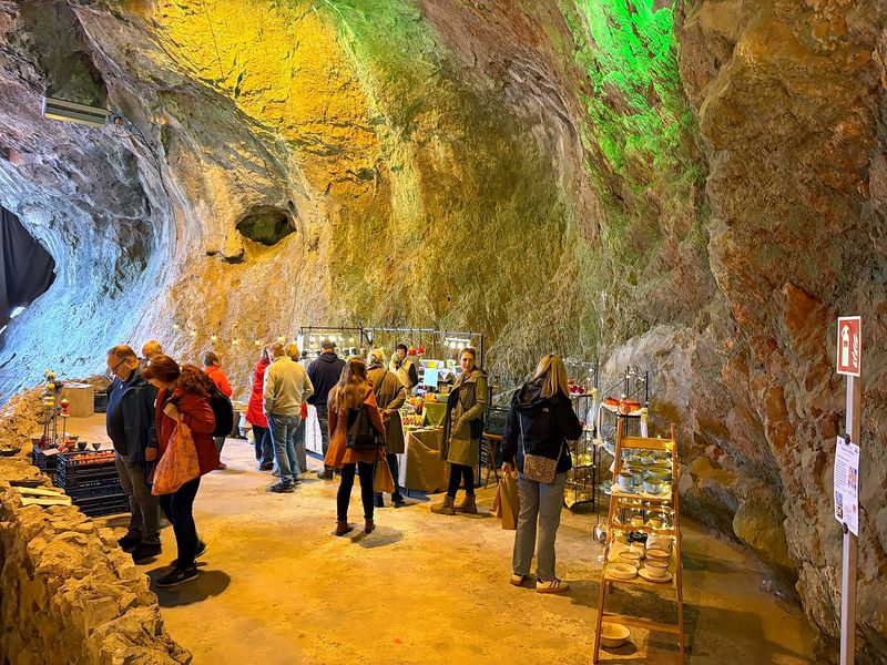 Keramikstand vor der grün und gelb beleuchteten Felswand, davor Besucher