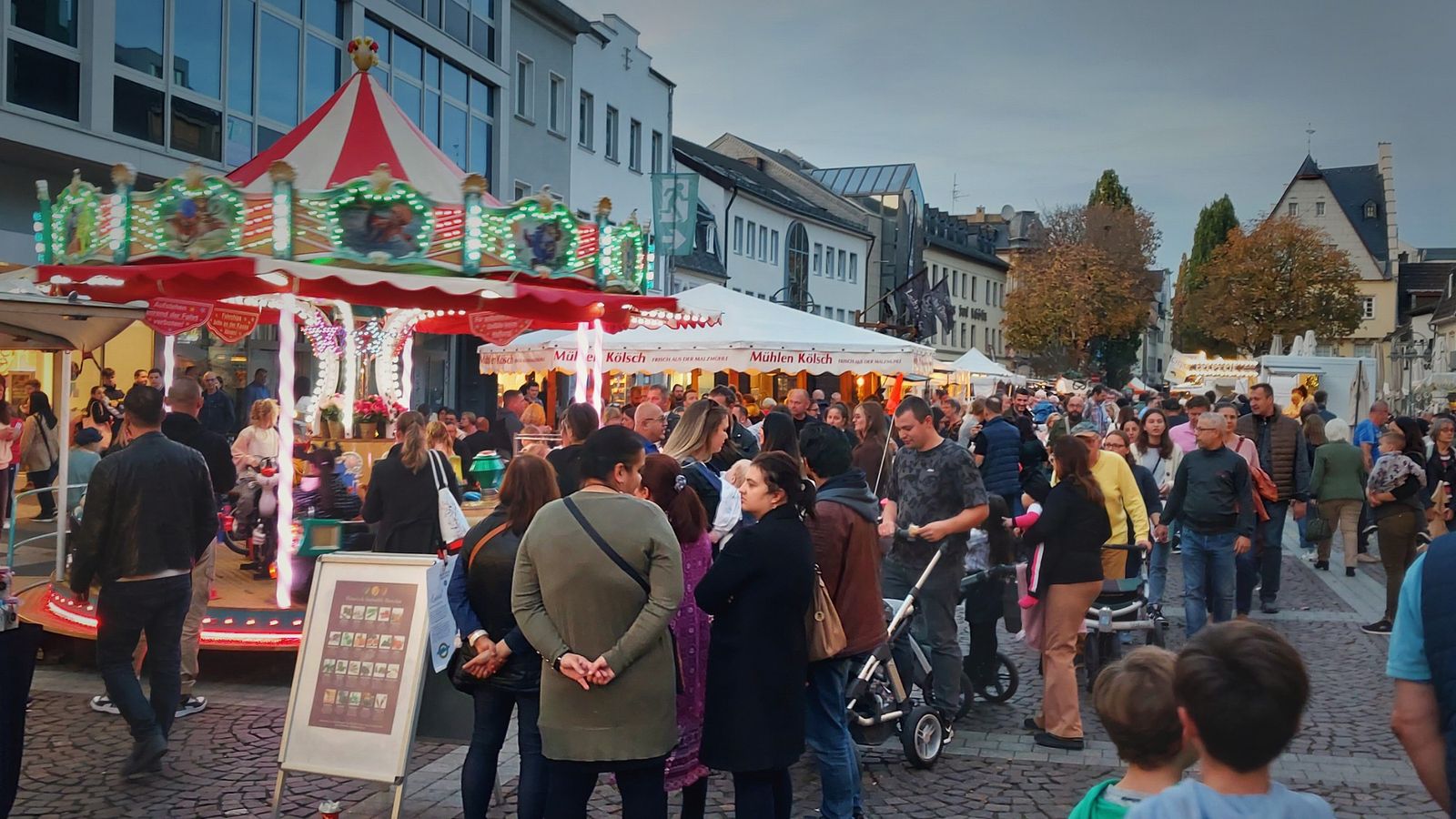 Belebter Herbstmarkt in einer Fußgängerzone mit Karussell, Marktständen und vielen Besuchern