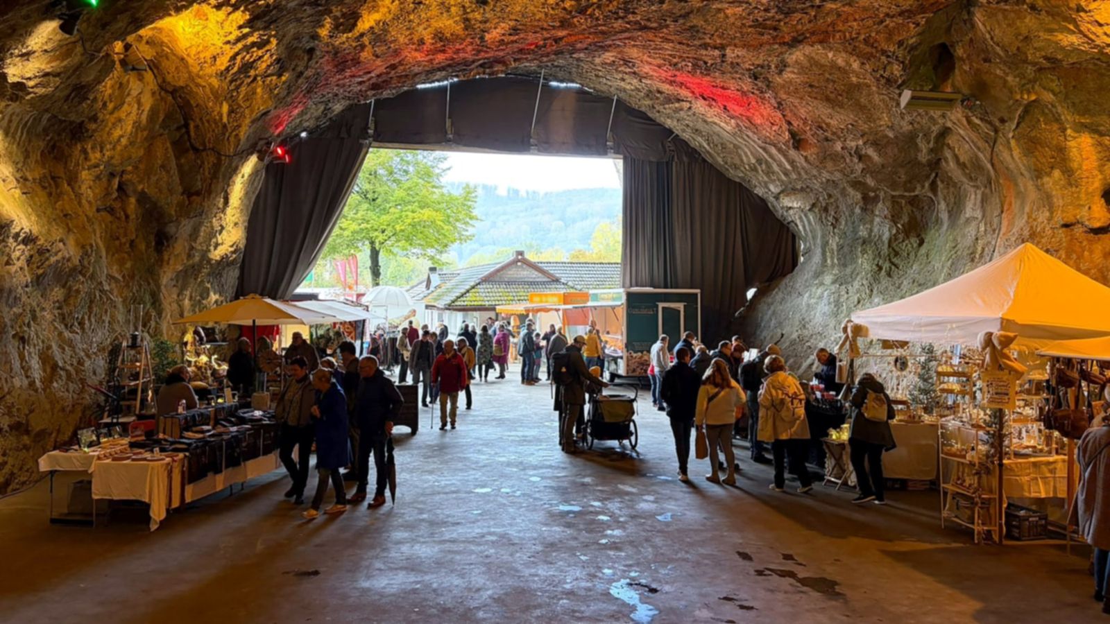 Kunsthandwerkermarkt in der Balver Höhle: Marktstände und Besucher unter dem farbig beleuchteten Felsgewölbe, hinten der Höhleneingang